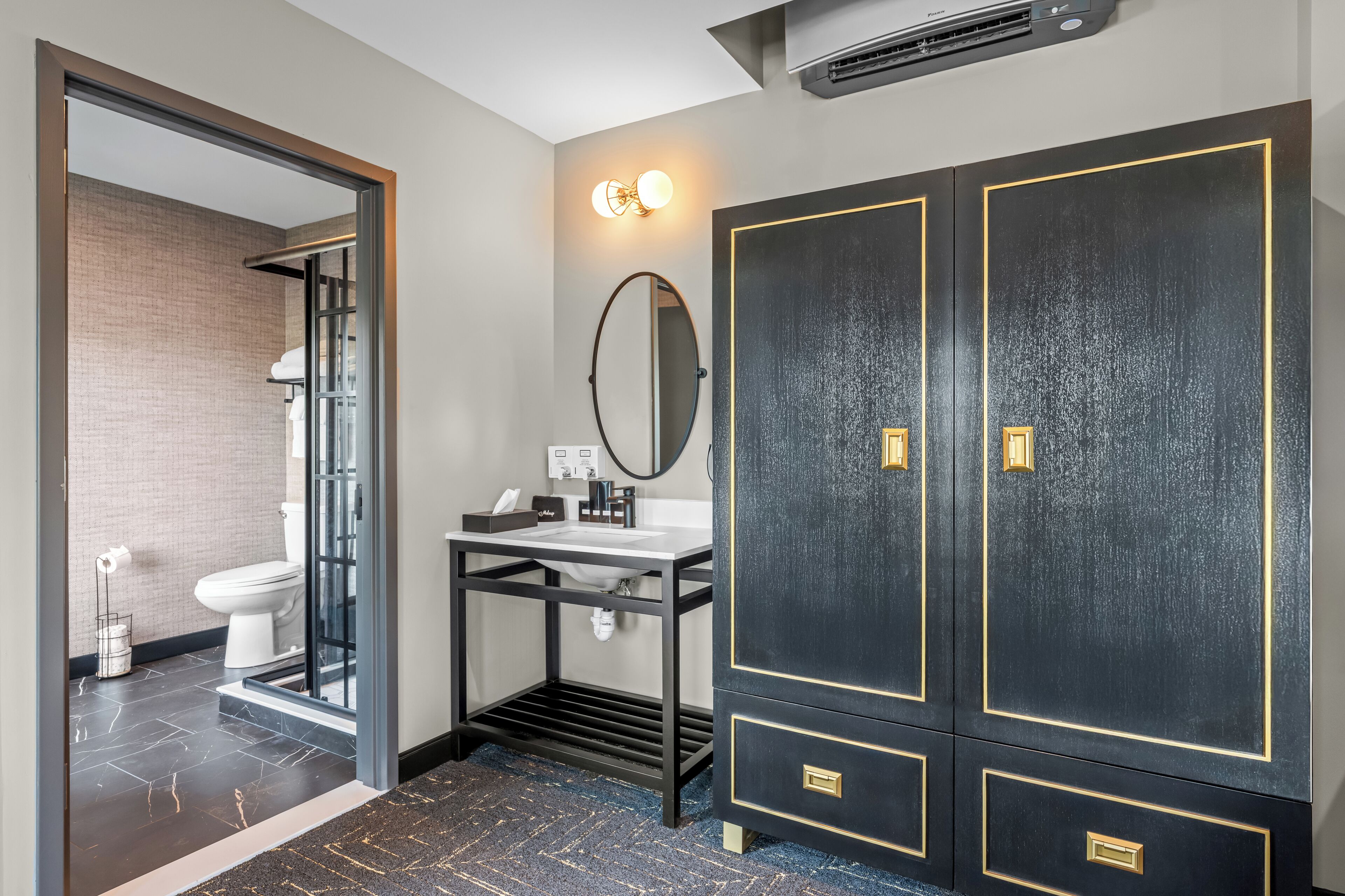 Ein modernes Badezimmer mit Duschkabine aus Glas, einem Waschbecken mit Spiegel und einem dunklen Kleiderschrank mit goldenen Akzenten.