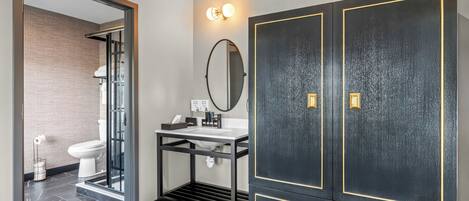 A modern bathroom with a glass shower enclosure, a sink with a mirror, and a dark wardrobe with gold accents.