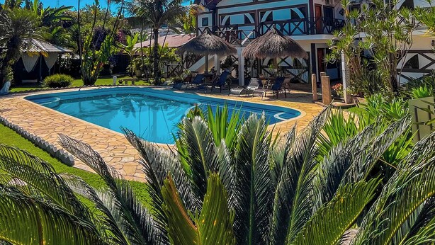 A pool area with a clear blue sky, palm trees, and a building with a balcony. - Pousada Igarapé (Socorro)