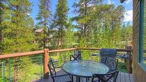 A wooden deck with a glass table and chairs, surrounded by a metal railing, overlooking a forested area. - Premier Keystone 3BR Townhome w/ Resort Access (Keystone)