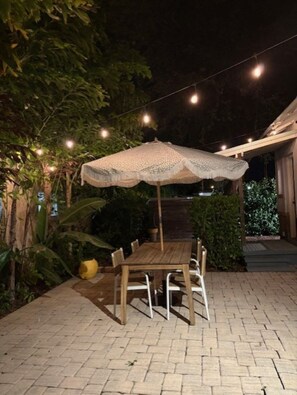 Un patio al aire libre con una mesa y sillas de madera, una sombrilla y luces colgantes.