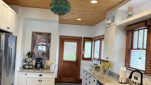 Une cuisine moderne avec un plafond en bois, des comptoirs en granit, des appareils électroménagers en acier inoxydable et un îlot central doté d’un évier.