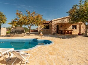 A pool area with a stone floor, a covered seating area, and a stone building with a tiled roof. - Holiday House Šimun (Stankovci)