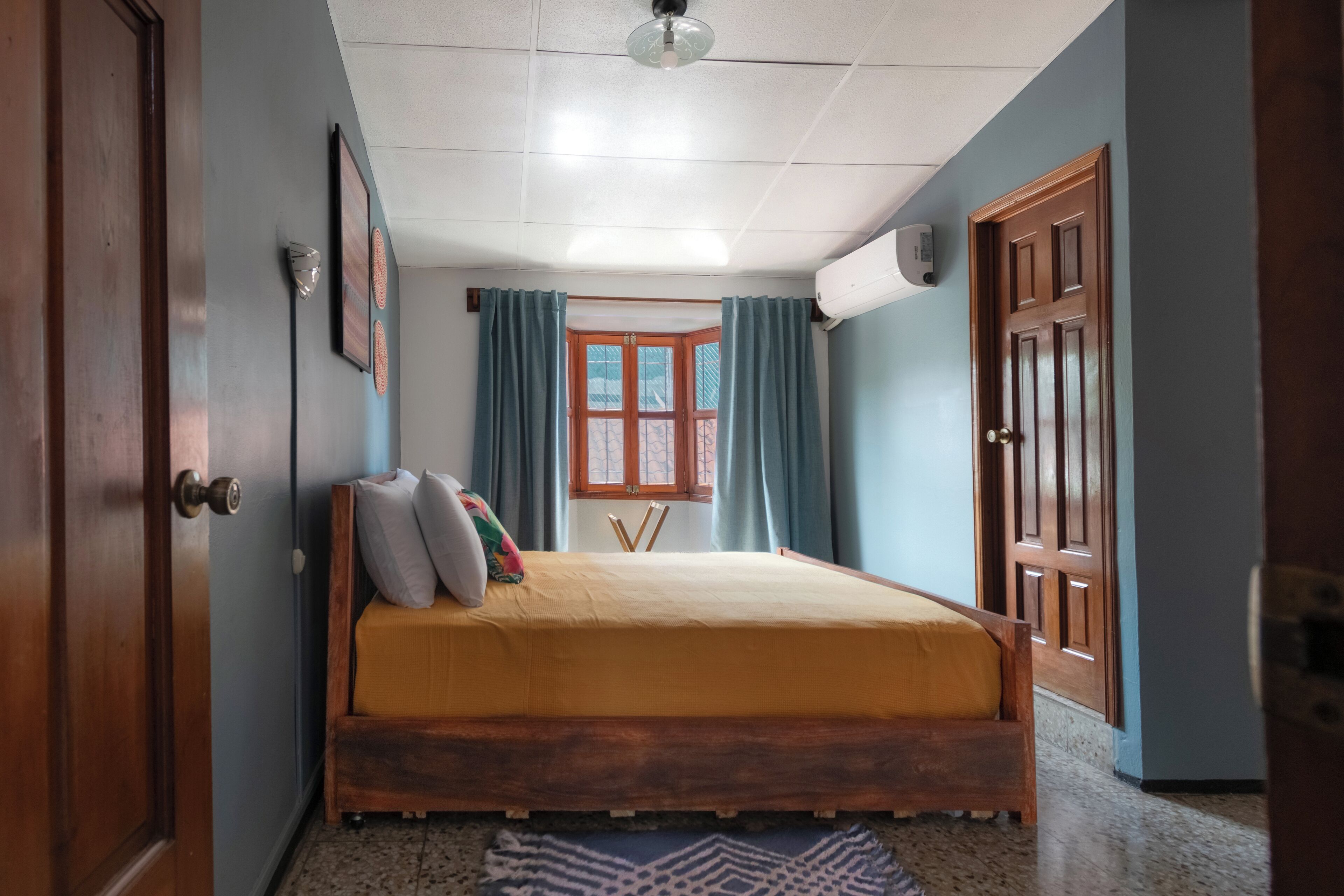 Ein Schlafzimmer mit einem Bett, einem Vorhangfenster, einem Deckenventilator und Holztüren.