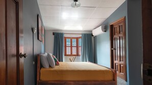 Ein Schlafzimmer mit einem Bett, einem Vorhangfenster, einem Deckenventilator und Holztüren.