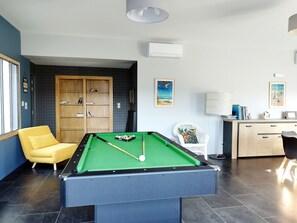 A pool table with a green felt surface, a yellow armchair, a wooden cabinet, and a desk with a lamp.