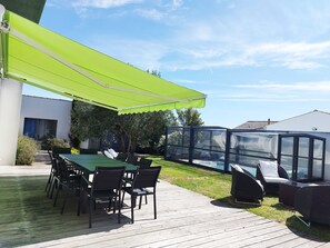 A patio with a green awning, a pool, and outdoor furniture.