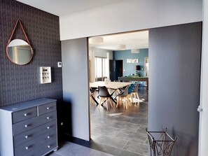 A modern interior with a dining area, a mirror, a wall-mounted control panel, and a staircase.