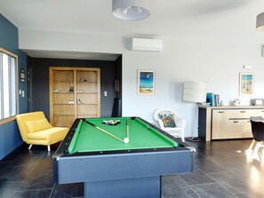 A pool table with a green felt surface, a yellow armchair, a wooden cabinet, and a desk with a lamp.