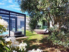 A glass-enclosed room with a view of a swimming pool, a grassy outdoor area with a dining table and chairs, and a large tree. - 4* villa with indoor swimming spa, billiards (Aytré)