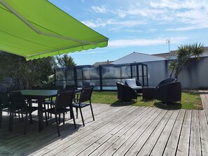 A wooden deck with outdoor furniture, a glass enclosure, and a green awning.