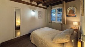 A bedroom with a wooden ceiling, a bed with a white bedspread, a nightstand with a lamp, a window with curtains, and a wall-mounted mirror. - T3 duplex house, atypical, with wooded garden, very large terrace and parking space (Toulouse)