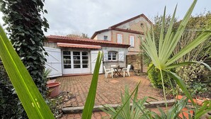 A house with a tiled roof, a brick patio, and a garden with potted plants and a table with chairs. - T3 duplex house, atypical, with wooded garden, very large terrace and parking space (Toulouse)
