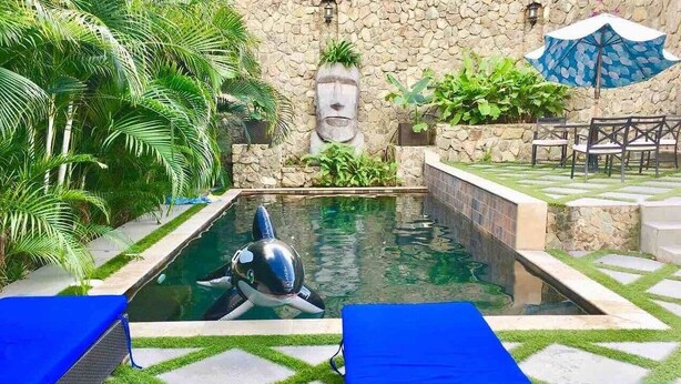 A pool area with a dolphin statue, blue lounge chairs, and a stone wall with greenery. - Centrally located Simpson bay 1bdr apt (1-4A) (Simpson Bay)