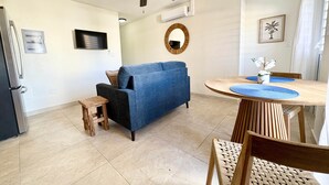 A modern living room with a blue sofa, a wooden dining table with blue placemats, a ceiling fan, and a small wooden stool. - Centrally located Simpson bay 1bdr apt (1-4A) (Simpson Bay)
