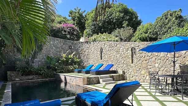 A pool area with lounge chairs and a stone wall. - Modern apartment with shared pool and generator (2-2B) (Simpson Bay)