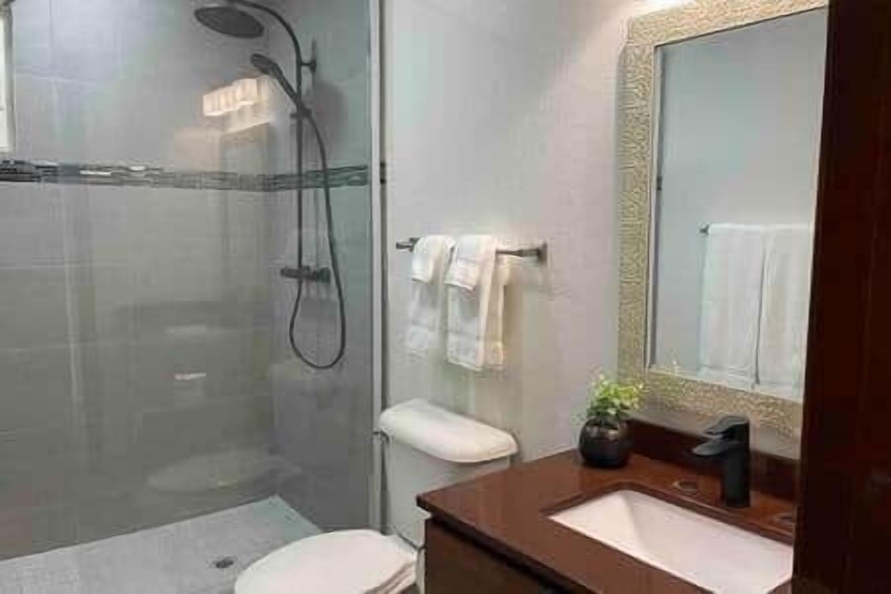 A modern bathroom with a glass-enclosed shower, a white toilet, a sink with a dark faucet, and a mirror with a decorative frame.