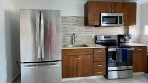 A modern kitchen with stainless steel appliances, wooden cabinets, and a tiled backsplash. - Modern apartment with shared pool and generator (2-2B) (Simpson Bay)