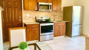 A modern kitchen with wooden cabinets, stainless steel appliances, and a glass table with a plant. - Blue Sky Apt in the middle of Simpson Bay-GENERATOR(1-3A) (Simpson Bay)