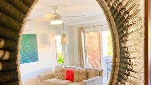 A mirror with a woven frame reflecting a living room with a beige sofa, a red pillow, and a ceiling fan. - Blue Sky Apt in the middle of Simpson Bay-GENERATOR(1-3A) (Simpson Bay)