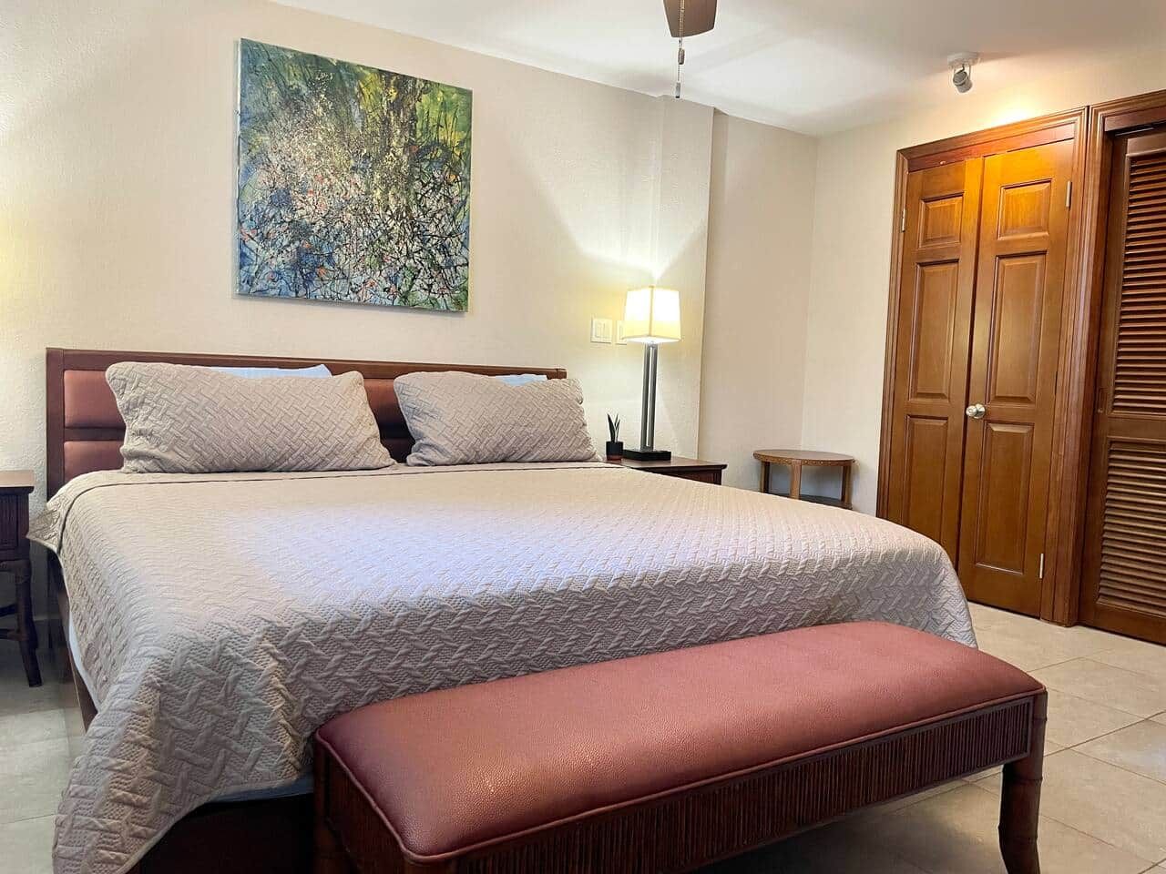 Un lit bien fait, avec une tête de lit, une lampe de chevet et une porte en bois en arrière-plan.