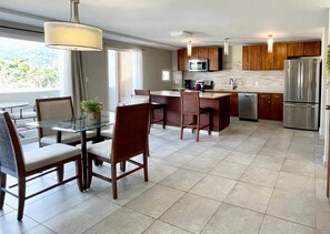 A modern kitchen with a dining area, featuring a glass table, wooden chairs, and a stainless steel refrigerator.
