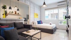 Una sala de estar moderna con un sofá, una mesita de centro y una cama. Hay lámparas colgantes, un estante con plantas y una ventana con vistas.