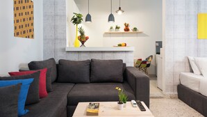 A modern living room with a grey sofa, a coffee table with a book and a plant, and a white shelf with decorative items. - Garage Studio in Mar Mikhael (Beirut)