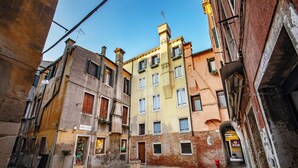 A narrow street with buildings on either side, featuring a mix of architectural styles and a small square in the center. - Daplace - Antica Casa Coppo  (Venice)