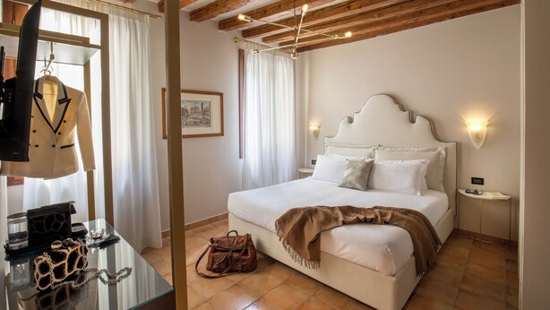 A bedroom with a bed, bedside table, and a hanging coat rack. - Daplace - Antica Casa Coppo  (Venice)
