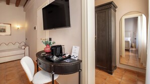 A hotel room with a flat-screen TV mounted on the wall, a dark wooden cabinet, a round table with a coffee maker, a white chair, and a large mirror. - Daplace - Antica Casa Coppo  (Venice)