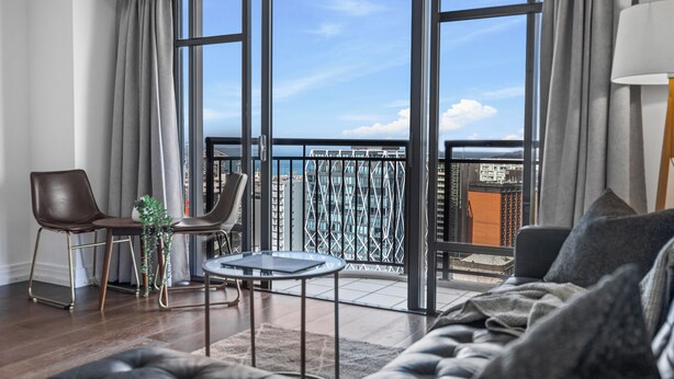 Un salon moderne doté d’une grande porte-fenêtre coulissante donnant sur un balcon avec vue sur la ville.