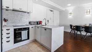 Une cuisine moderne avec des meubles blancs, un four encastré et un coin repas comprenant une table et des chaises.