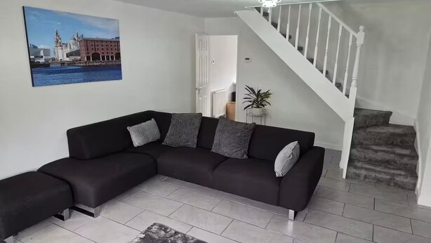 Uma sala de estar moderna com um sofá modular preto, uma pintura grande de uma paisagem urbana, uma escada e um vaso com planta.