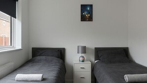Um quarto com duas camas de solteiro, uma mesa de cabeceira com abajur e um criado-mudo.