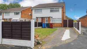 Um imóvel residencial com uma casa de dois andares, um jardim frontal e uma entrada para carros.