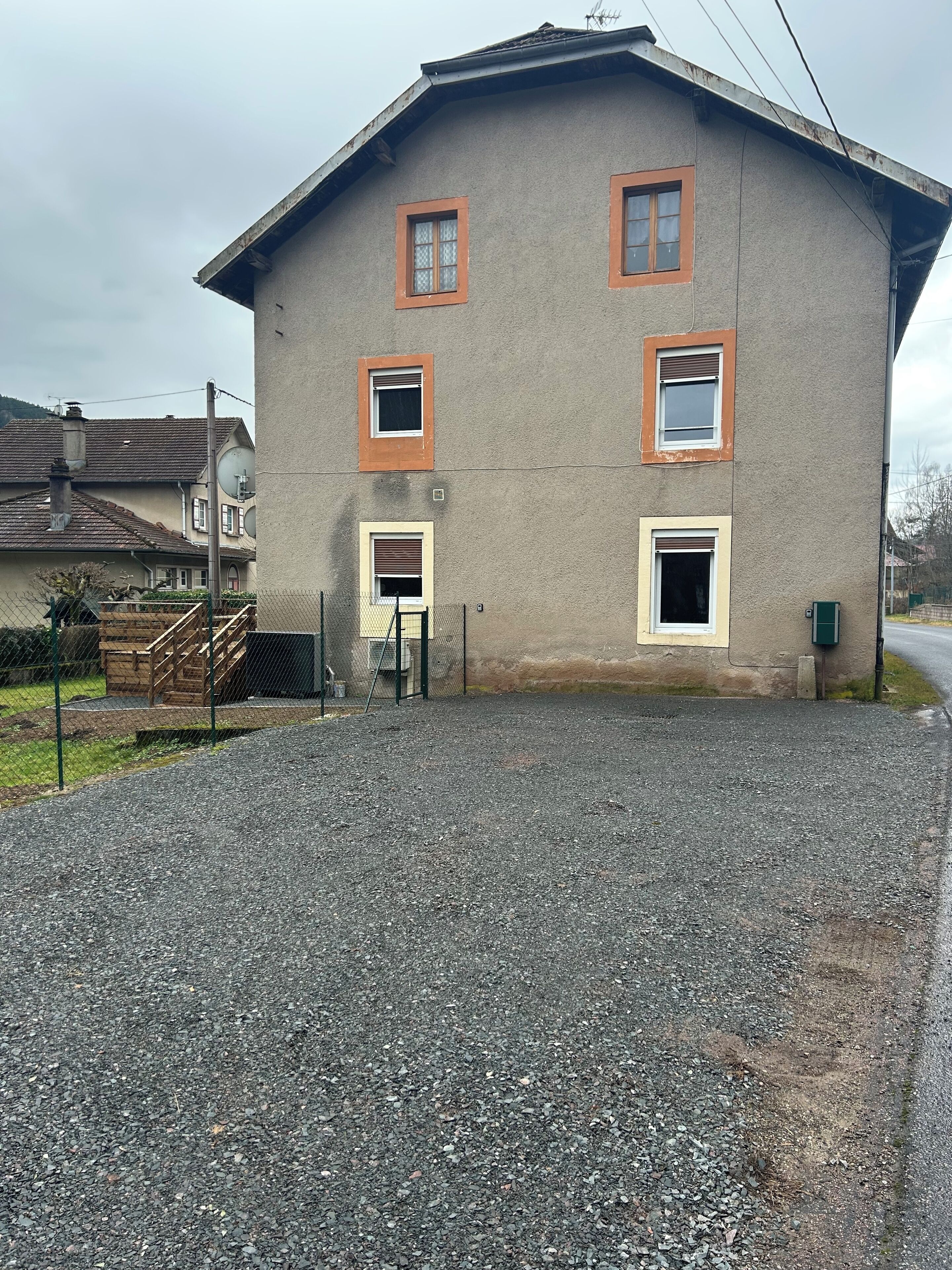 A two-story building with multiple windows, a gravel driveway, and a wooden fence.