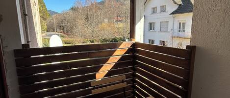 A balcony with a wooden bench and a table, overlooking a residential area and hills.