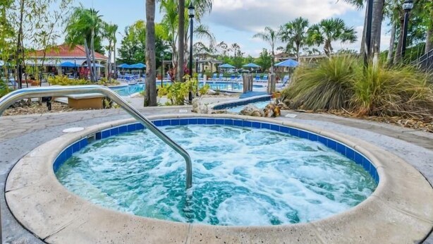 A hot tub with a metal ladder, surrounded by palm trees and a pool area. - Resort Style Kissimmee Home with Screened Pool Hot Tub and BBQ Near Disney World (Kissimmee)