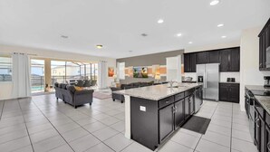 A spacious kitchen with a central island, dark cabinetry, and a large dining area with a sofa and table. - Stunning Kissimmee Home  Private Pool Near Disney Parks (Kissimmee)