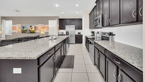 A modern kitchen with dark cabinetry, granite countertops, and stainless steel appliances. - Stunning Kissimmee Home  Private Pool Near Disney Parks (Kissimmee)