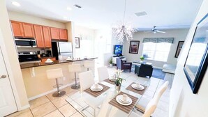 A modern kitchen with wooden cabinets, a built-in oven, and a dining area with a glass table and white chairs. - 5BR Pool+Hot Tub Home Kissimmee Near Disney WDW (Kissimmee)