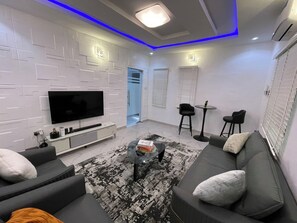 A modern living room with a flat-screen TV, black and white patterned rug, grey sofa, and black chairs. - Luxury Stay in Lagos (Lagos)
