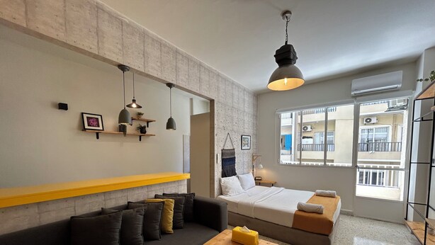 Ein moderner, kompakter Wohnraum mit Sofa, Bett, Holztisch und einer hängenden Pendelleuchte.