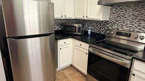 A kitchen with white cabinets, a stainless steel refrigerator, a microwave, a stove, and a tiled backsplash. - Nice 2 bedroom home with backyard only 15 mins outside of Atlanta. (Detroit)