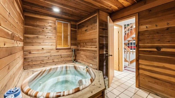 Una cabaña de madera con jacuzzi, paredes de madera, una ventana y una escalera que sube a un nivel superior.