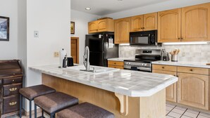 Una cocina moderna con armarios de madera, un refrigerador negro, un microondas y una isla grande con taburetes de bar.