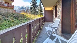 Ein Balkon mit zwei weißen Stühlen, einer Steinmauer und Blick auf Bäume und Berge.