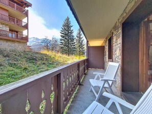 A balcony with two white chairs, a stone wall, and a view of trees and mountains. - 100m from ski slopes, Ground floor, swimming pool, balcony, tv, ski locker, 50m², Les Menuires (Les Menuires)