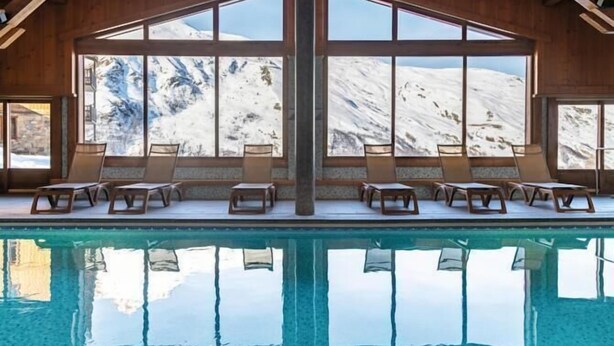 Ein Pool mit Liegestühlen und großen Fenstern, die einen Blick auf die Berge bieten.